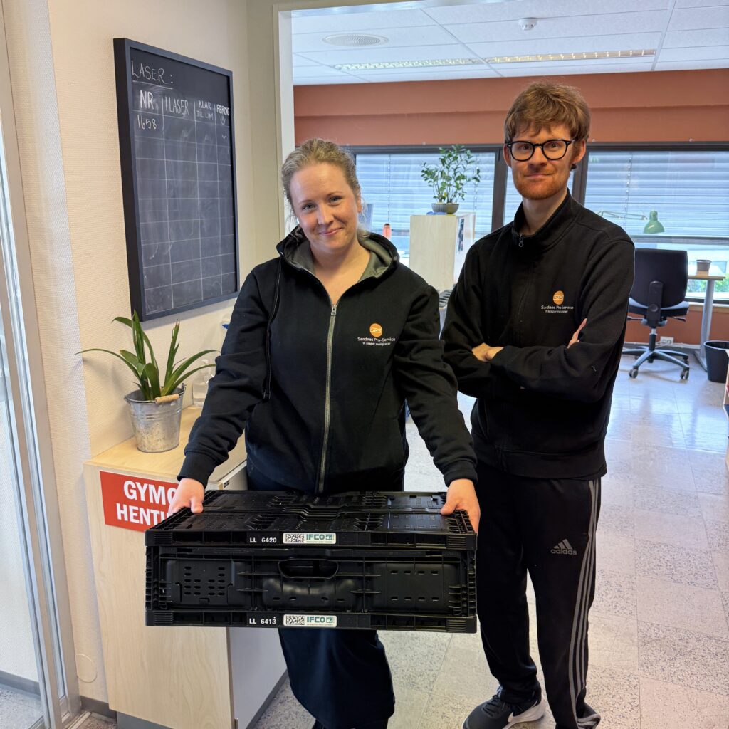 En dame som holder en kasse ved siden av en mann som står med armene i kryss.